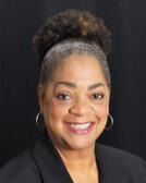 Professional Headshot Black woman with gold hoop hearings, natural hair in a loose bun wearing black blazer